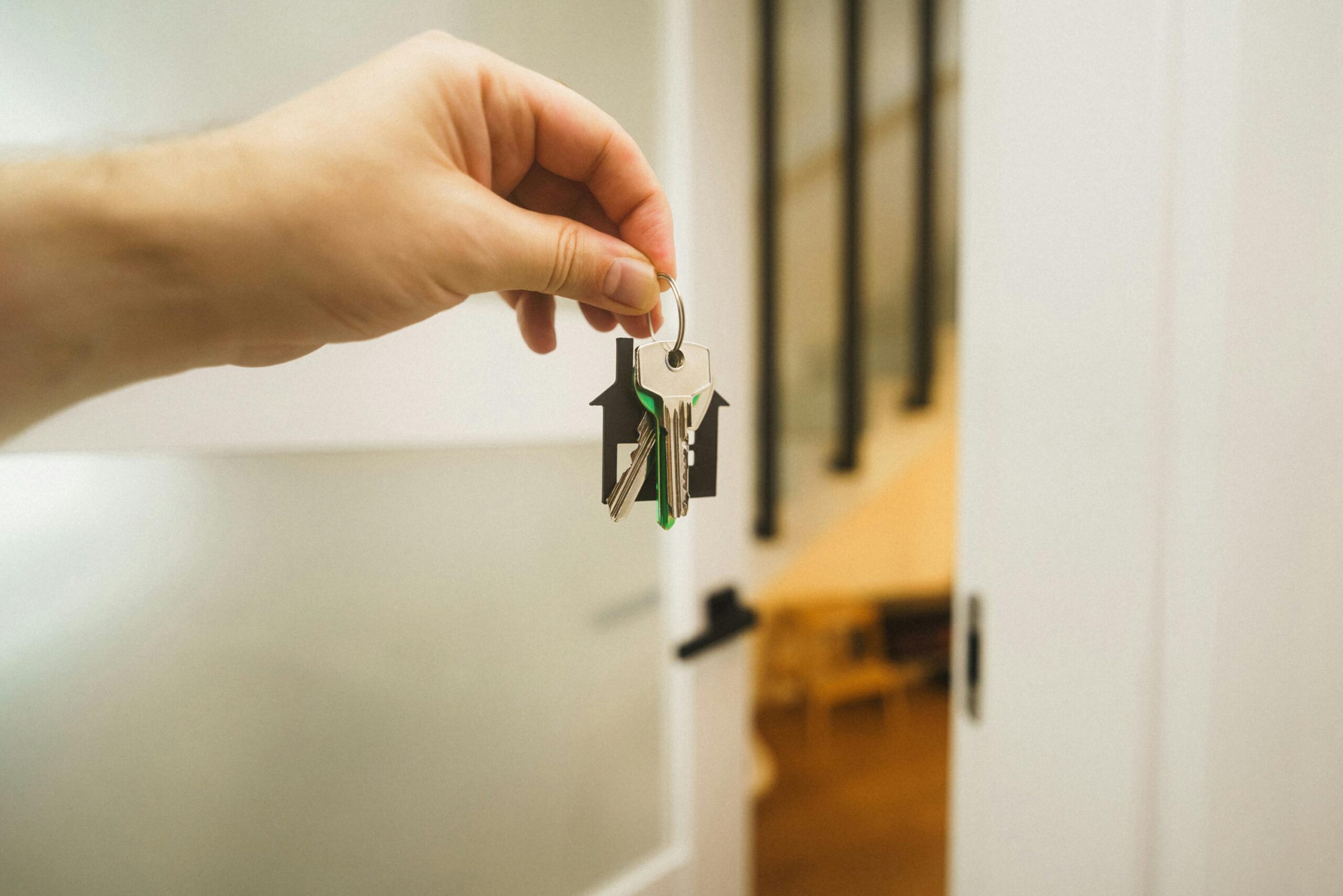 A hand holding a house key indoors signifies new ownership or leasing in real estate.